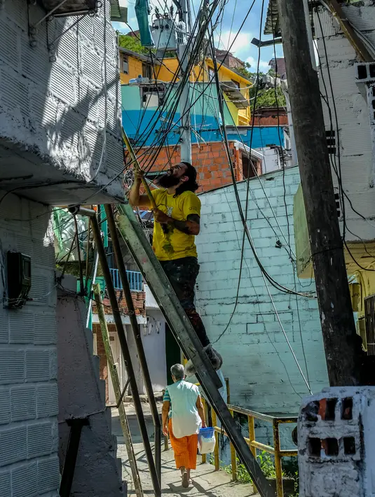 Seorang pria mengecat dinding bangunan di kawasan kumuh El Pesebre, pinggiran kota Medellin, Kolombia, 19 Juni 2017. Seniman Prancis, Tarik Bouanani melukis 230 rumah di kawasan tersebut membentuk mural raksasa. (JOAQUIN SARMIENTO/AFP)