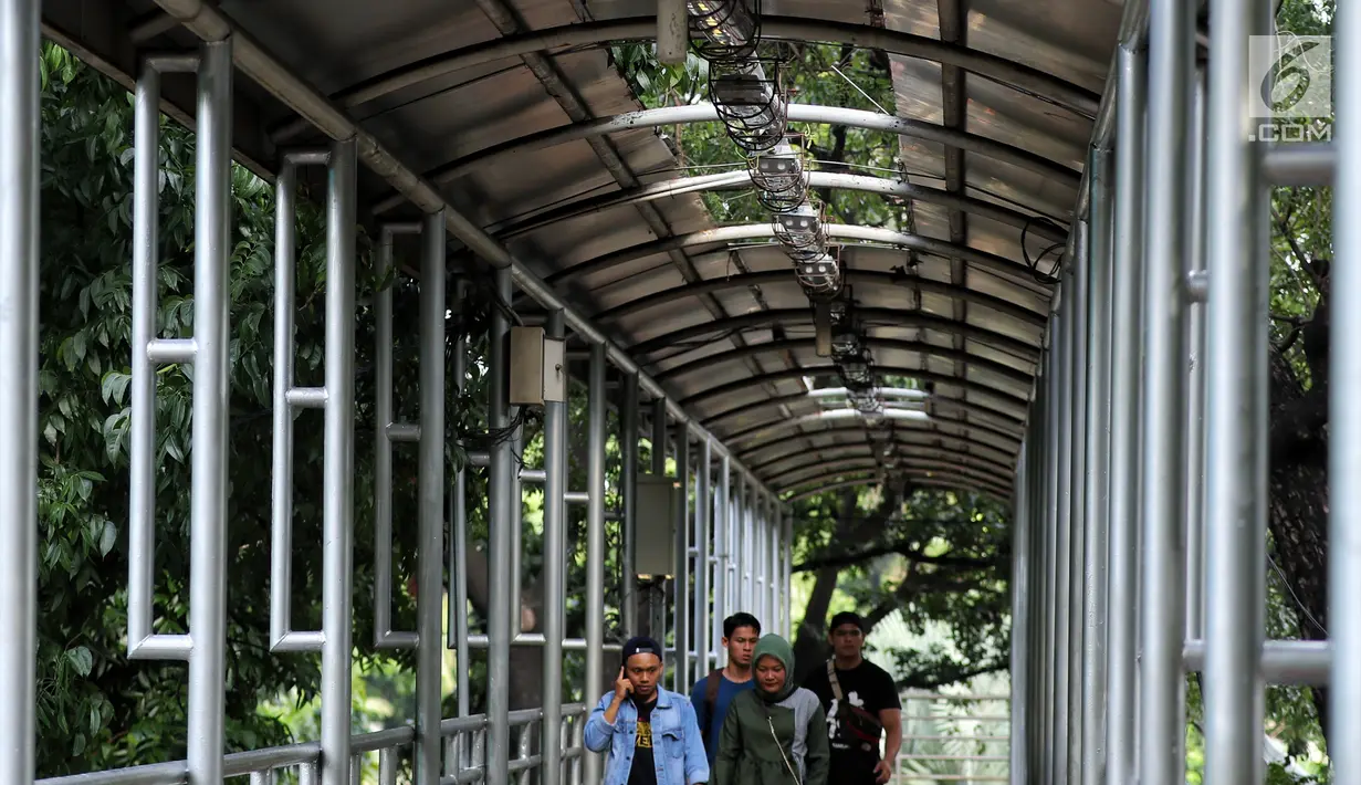 Pejalan kaki menyebrang di JPO Medan Merdeka Barat yang atapnya rusak di Jakarta, Jumat (19/1). Kondisi JPO yang penuh dengan genangan air dan atap yang rusak mengurangi kenyamanan bagi para pejalan kaki yang menggunakannya. (Liputan6.com/Johan Tallo)