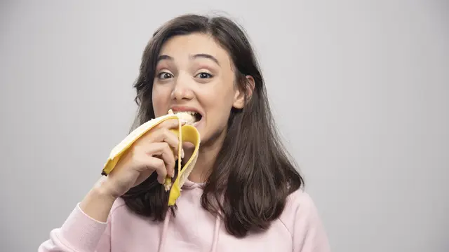 Seorang perempuan sedang menggigit sebuah pisang (Foto Dok: Freepik/azerbaijan_stockers)