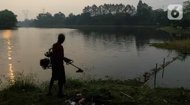 Warga memotong rumput di situ Sawangan di kawasan Sawangan, Depok, Jawa Barat, Kamis (27/7/2023). (Liputan6.com/Herman Zakharia)