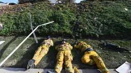 Petugas pemadam kebakaran berbaring di atas tanah setelah kelelahan mengatasi kebakaran yang disebut Lilac Fire di Bonsall, California, Jumat (8/12). Negara bagian tesebut memberlakukan keadaan darurat yang dipicu oleh kebakaran hutan. (Robyn Beck/AFP)