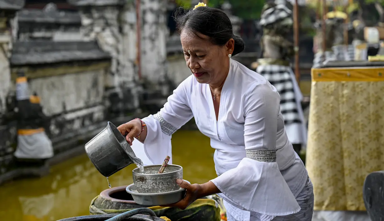 Seorang perempuan menuangkan air suci ke dalam mangkuk saat Hari Raya Galungan di sebuah pura di Bali, Rabu (4/1/2023). Perayaan Hari Galungan merupakan hari kemenangan kebenaran (Dharma) atas kejahatan (Adharma). (SONNY TUMBELAKA / AFP)