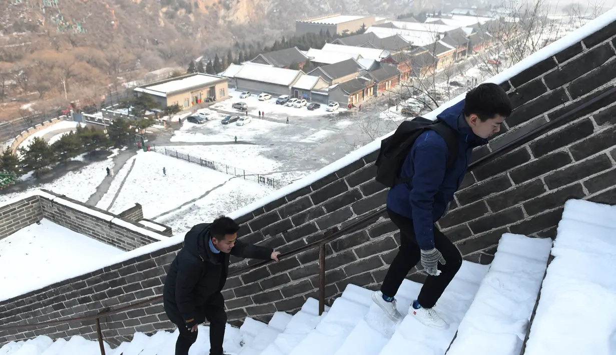 Dua wisatawan menaiki anak tangga saat menikmati liburan musim dingin di Tembok Besar China yang diselimuti salju di utara Beijing (6/1/2020). Salju yang turun tidak menyurutkan para wisatawan baik lokal maupun dari mancanegara untuk berkunjung ke Tembok Besar China. (AFP/Greg Baker)