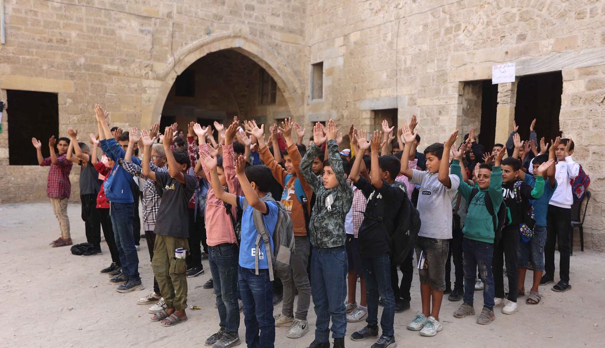 Anak-anak Palestina berdiri di halaman sekolah bersejarah "Al-Kamaliya al-Othmanya" saat mereka berolahraga sebelum masuk sekolah di Kota Tua Gaza yang menjadi bagian dari inisiatif sukarelawan yang diorganisir oleh para guru pengungsi, di Kota Gaza pada 2 November 2025. Banyak di antaranya kini dialihfungsikan menjadi tempat penampungan darurat yang menampung puluhan ribu pengungsi. (Omar AL-QATTAA/AFP)