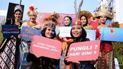 Petugas berpakaian adat daerah menunjukkan tulisan saat social community gathering Satgas Saber Pungli di Jakarta, Minggu (17/9). Kemenko Polhukam meluncurkan maskot dan melakukan sosialisasi satgas saber pungli. (Liputan6.com/Helmi Fithriansyah) 