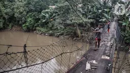 Anak-anak melintasi jembatan gantung yang sudah tidak layak di kawasan Srengseng Sawah, Jakarta, Sabtu (12/6/2021). Jembatan gantung tersebut hanya mengandalkan ikatan tambang besi yang mengait pada beton dan pepohonan yang ada di sekitar kali. (merdeka.com/Iqbal S. Nugroho)