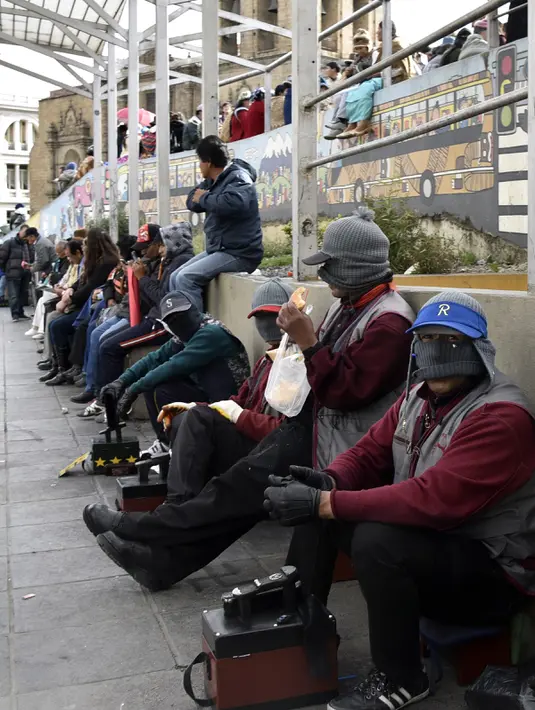 Para tukang semir sepatu bertopeng menunggu pelanggan di kawasan La Paz, Bolivia (29/11). Karena diantara mereka masih ada yang menjalani pendidikan di sekolah dan universitas para tukang semir ini menutup wajahnya. (AFP PHOTO/Aizar Raldes)
