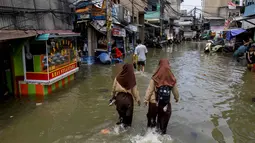 Banjir rob di kawasan Muara Baru Jakarta merupakan fenomena yang terjadi akibat pasang tinggi air laut yang bersamaan dengan kondisi cuaca tertentu. Tampak dalam foto, dua siswi mengarungi jalan yang terendam banjir akibat pasang tinggi di Muara Baru, Jakarta, pada Sabtu 6 Desember 2025. (ADITYA IRAWAN/AFP)
