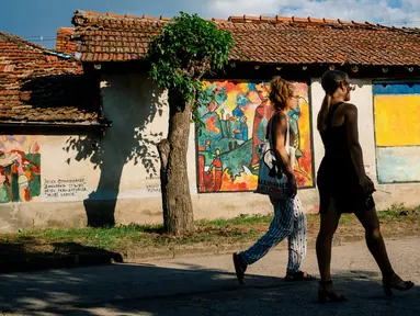 Dua orang wanita melewati lukisan mural karya seniman terkenal di dinding rumah desa Staro Zhelezare di Bulgaria, 4 Agustus 2018. Dengan populasi penduduk dibawah 500 orang, desa ini disulap menjadi galeri seni yang penuh mural. (AFP/Dimitar DILKOFF)