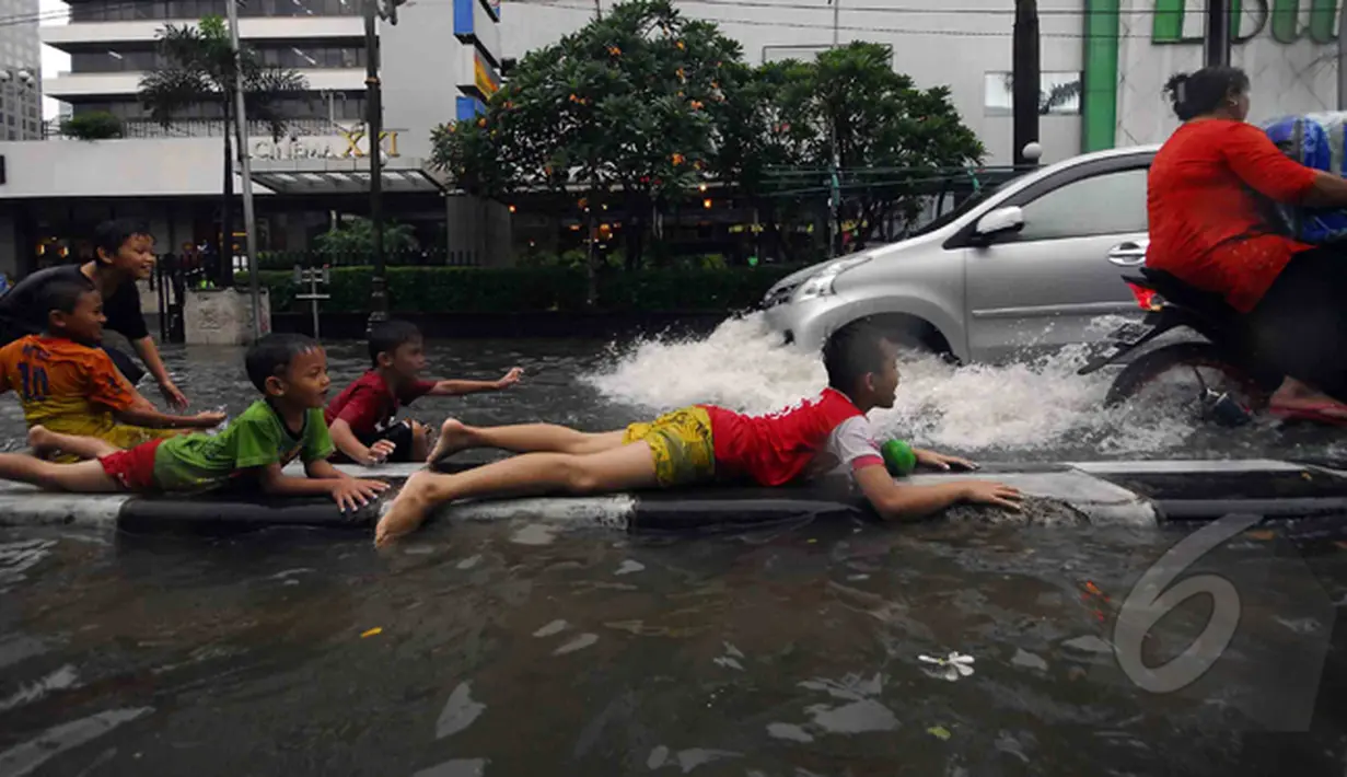 Sejumlah bocah asyik bermain di pembatas jalan saat banjir melanda kawasan Sarinah, Jakarta, Senin (9/2/2015). (Liputan6.com/Johan Tallo)
