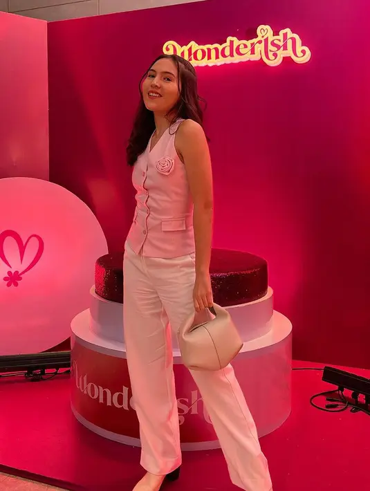 Olivia Jensen mengenakan vest pink dengan aksen bros bunga mawar dipadukan celana putih panjang. [@oliviajensen]