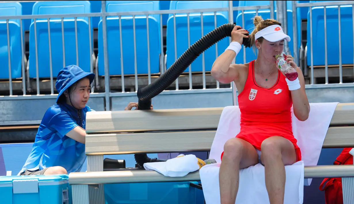 Petenis Serbia Nina Stojanovic mendinginkan tubuhnya dengan mesin pendingin dalam pertandingan tenis putaran pertama tunggal putri Olimpiade Tokyo 2020 melawan Nao Hibino di Ariake Tennis Park, Tokyo, Sabtu (24/7/2021). (Foto: AFP/Giuseppe Cacace)