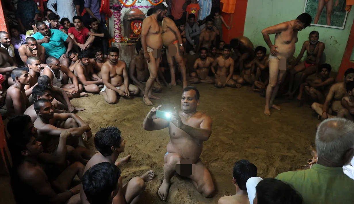 Seorang pegulat saat memfoto pegulat lainnya sebelum bertanding di festival Nag Panchami di Allahabad, India, (7/8). Festival ini diadakan selama musim hujan dengan doa dan upeti untuk ular. (AFP PHOTO/SANJAY Kanojia)