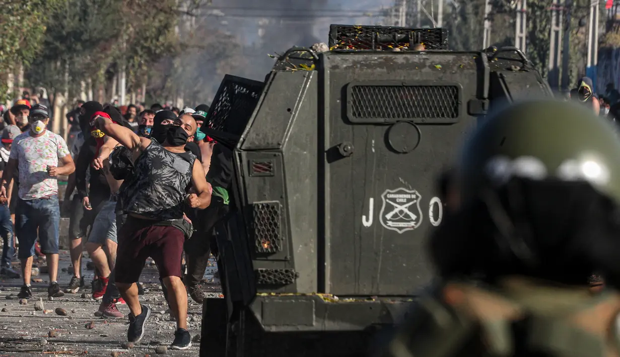 Demonstran melempar batu saat saat bentrok dengan polisi di tengah pandemi virus corona Covid-19 selama penguncian wilayah (lockdown) di lingkungan miskin di Santiago, Chili, (18/5/2020). (AP Photo/Esteban Felix)