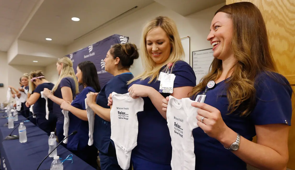 Paige Packard dan Allison Thompson memegang pakaian bayi ketika konferensi pers bersama 16 suster di bagian gawat darurat sebuah rumah sakit di Mesa, Arizona yang sedang hamil pada periode yang relatif bersamaan, 17 Agustus 2018. (AP/Ross D. Franklin)