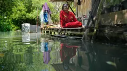 Munadiroh duduk di luar rumahnya di Mondoliko, Jawa Tengah, Indonesia, 1 Agustus 2022. Anaknya menempuh perjalanan jauh ke sekolah dengan mengarungi air dan naik perahu beberapa kali dalam seminggu. (AP Photo/Dita Alangkara)