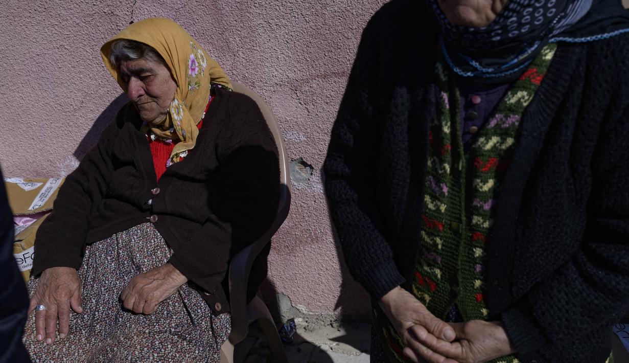 Warga lanjut usia menunggu saat yang lain mengambil makanan dan pakaian yang dikirim dari belakang truk di Samandag, selatan Hatay pada 16 Februari 2023, sepuluh hari setelah gempa berkekuatan 7,8 melanda wilayah perbatasan Turki dan Suriah. Lusinan tangan dengan panik meraih pemanas dan selimut yang dibagikan oleh donor swasta, menggambarkan keputusasaan dan kemarahan yang mencengkeram wilayah Turki 11 hari setelah bencana gempa. (Photo by Yasin AKGUL / AFP)