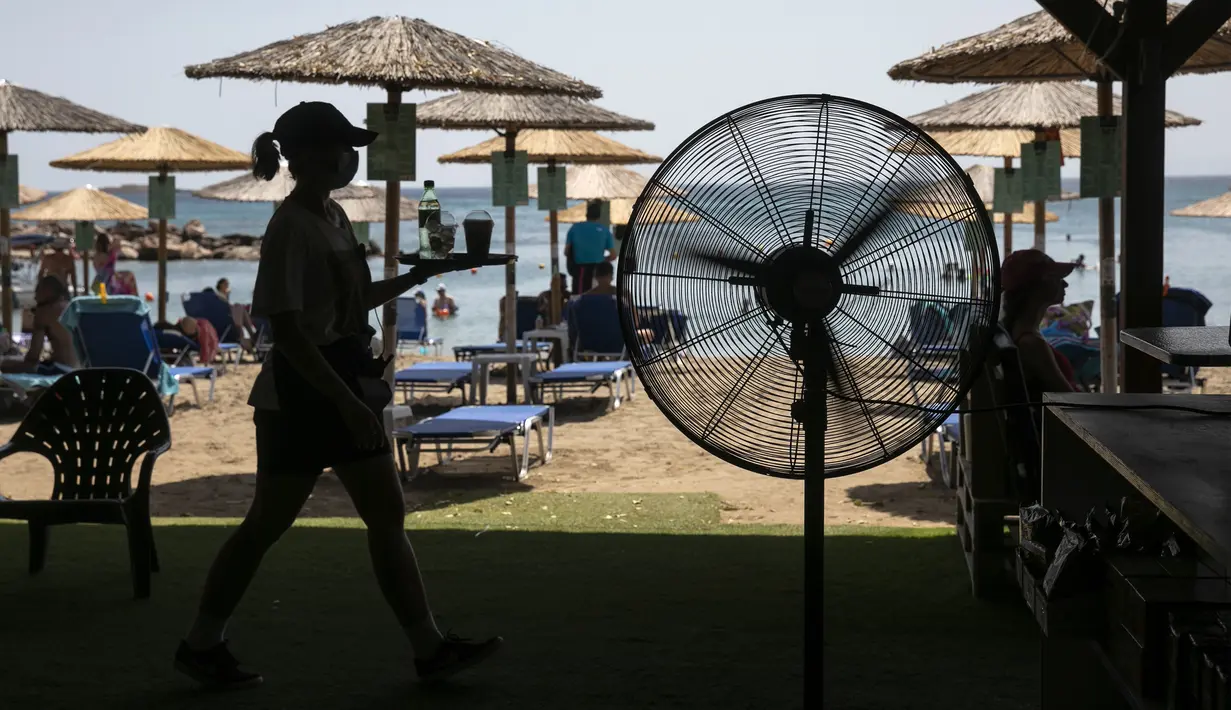 Seorang pelayan menyajikan minuman di bar pantai Desa Lagonissi, beberapa mil barat daya Athena, Yunani, Kamis (29/7/2021). Salah satu gelombang panas paling parah yang tercatat sejak 1980-an melanda Eropa tenggara. (AP Photo/Yorgos Karahalis)