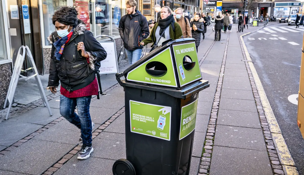 Pejalan kaki berjalan melewati tempat sampah untuk masker sekali pakai, di Aarhus Center, Denmark, Senin (23/11/2020). Kota Aarhus menempatkan seratus tempat sampah khusu berukuran 240 liter yang dapat menampung sekitar 3000 masker bekas. (Henning Bagger/Ritzau Scanpix/AFP)