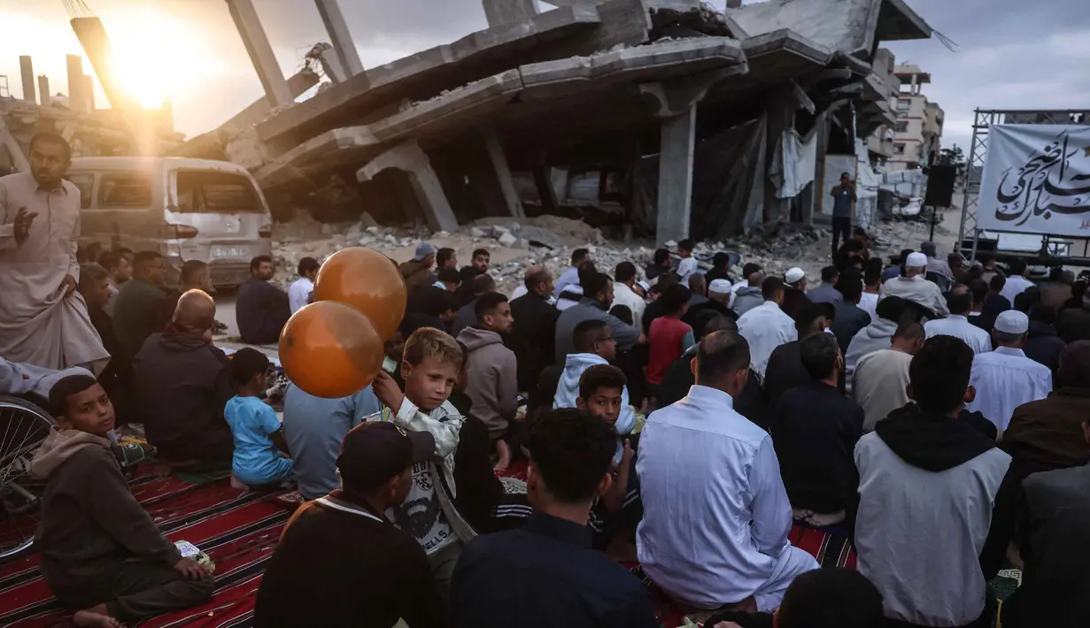 Seorang anak laki-laki memegang balon berdiri di antara warga Palestina yang berkumpul di jalan yang rusak parah untuk melaksanakan salat menandai dimulainya Idul Adha, Hari Raya Kurban, di Khan Yunis, Jalur Gaza Selatan, pada Rabu 27 Mei 2026. (BASHAR TALEB/AFP)
