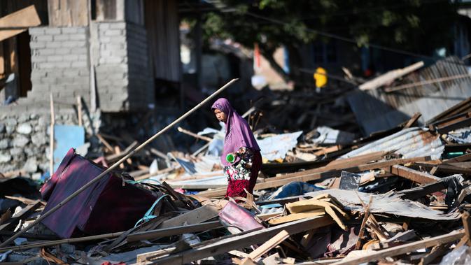Seorang wanita mencari barang-barang yang tersisa di antara puing rumah akibat gempa dan tsunami di Donggala, Sulawesi Tengah, Jumat (5/10). Gempa bumi berkekuatan 7,4 skala richter melanda Palu dan Donggala pada 28 September 2018 lalu. (AFP/Jewel SAMAD)