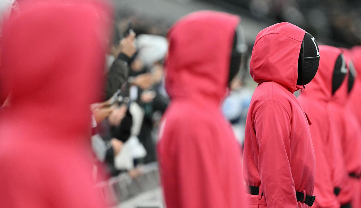 Orang-orang berpakaian seperti penjaga Squid Games dengan berdiri di area penonton selama pertandingan lanjutan Liga Inggris 2024/2025 antara Tottenham Hotspur melawan Liverpool di Stadion Tottenham Hotspur, London, Inggris Minggu (22/12/2024). Seperti diketahui, aksi tersebut ternyata merupakan promo musim kedua serial Korea Selatan tersebut. (AFP/Glyn Kirk)