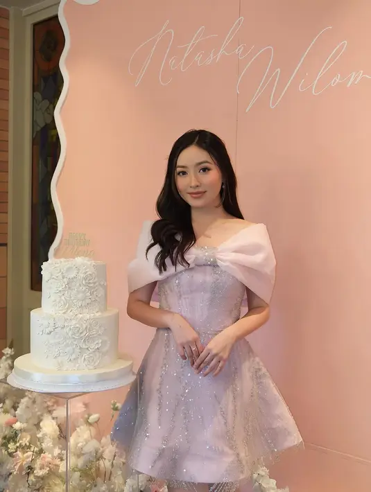 Natasha tampil memukau dalam balutan gaun karya @irenedanielle, yang menonjolkan siluet feminin dan detail yang lembut. Gaun pendek berwarna soft pink tersebut dihiasi aksen kilauan manik-manik yang memberikan sentuhan glamor tanpa berlebihan. [@natashawilona12].