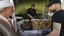 Pelanggan menunggu saat pedagang membuat falafel untuk hidangan berbuka puasa, selama bulan suci Ramadhan di pusat kota Hebron di Tepi Barat yang diduduki (9/4/2022). Makanan ini dibuat dari kacang Arab yang digiling dan kemudian dipadatkan dan dibuat bola-bola kecil lalu digoreng. (AFP/Hazem Bader)