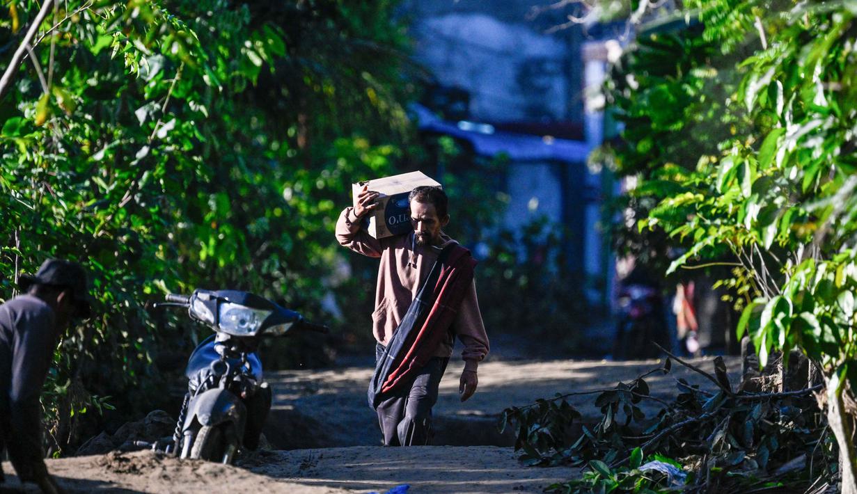 Hingga kini, akses darat ke Kecamatan Bandar Baru, Trienggadeng, dan Ulim masih terisolasi karena jembatan putus dan material longsor menutupi badan jalan. Tampak dalam foto, seorang warga mengangkut persediaan makanan di jalan yang tertutup lumpur setelah banjir bandang di Meureudu, Kabupaten Pidie Jaya, Provinsi Aceh, pada 29 November 2025. (CHAIDEER MAHYUDDIN/AFP)