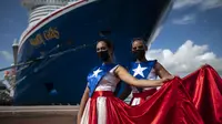 Ivanelis Jimenez (depan) dan Veronica Barreto mengenakan gaun bendera Puerto Rico saat menyambut penumpang kapal pesiar Mardi Gras Carnival yang berlabuh di Teluk San Juan, Puerto Rico, Selasa (3/8/2021). (AP Photo/Carlos Giusti)