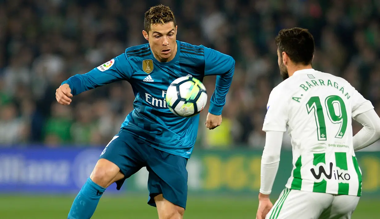 Pemain Real Madrid, Cristiano Ronaldo mengendalikan bola di hadapan pemain Real Betis, Bartra pada laga pekan ke-24 La Liga Spanyol, di Estadio Benito Villamarin, Minggu (18/2). Real Madrid menang dengan skor 5-3. (Cristina Quicler/AFP)