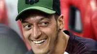 Gelandang Arsenal, Mesut Ozil tersenyum di bangku cadangan saat melihat rekannya bertanding melawan Atletico Madrid di International Champions Cup di Singapura (26/7). Arsenal kalah 3-1 setelah bermain 1-1 di waktu normal. (AP Photo/Yong Teck Lim)