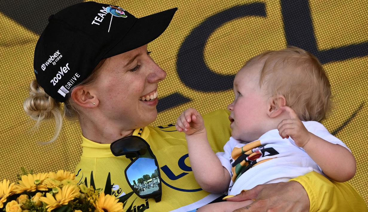 Pebalap Tim DSM, Lorena Wiebes menggendong anaknya saat merayakan kemenagannya di etape pertama Tour de France Wanita 2022 yang menempuh jarak sepanjang 81,6 km dari Tour Eiffel hingga Champs-Elysees, Paris pada 24 Juli 2022. (AFP/Jeff Pachoud)