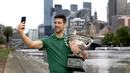 Petenis tunggal putra Serbia, Novak Djokovic melakukan swafoto bersama trofi Norman Brooks Challenge Cup setelah menjadi juara pada Australia Open 2023 di dekat sungai Yarra, Melbourne, Australia, Senin (30/01/2023). Djokovic berhasil mengalahkan petenis Yunani, Stefanos Tsitsipas di babak final dengan skor 6-3, 7-6(7-4), 7-6(7-5). (AFP/Fiona Hamilton)