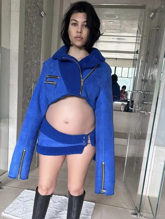 Kourtney memamerkan baby pumpnya dengan jaket crop top dan mini skirt warna biru dan sepatu boots hitamnya. @kourtneykardash