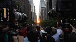 Orang-orang mengambil gambar saat matahari terbenam di Manhattan ketika fenomena "Manhattanhenge" di 42nd street, New York, Senin (11/7/2022). Fenomena Manhattanhenge hanyaterjadi di musim panas, tepatnya diantara bulan Mei hingga Juli. (Yuki IWAMURA / AFP)