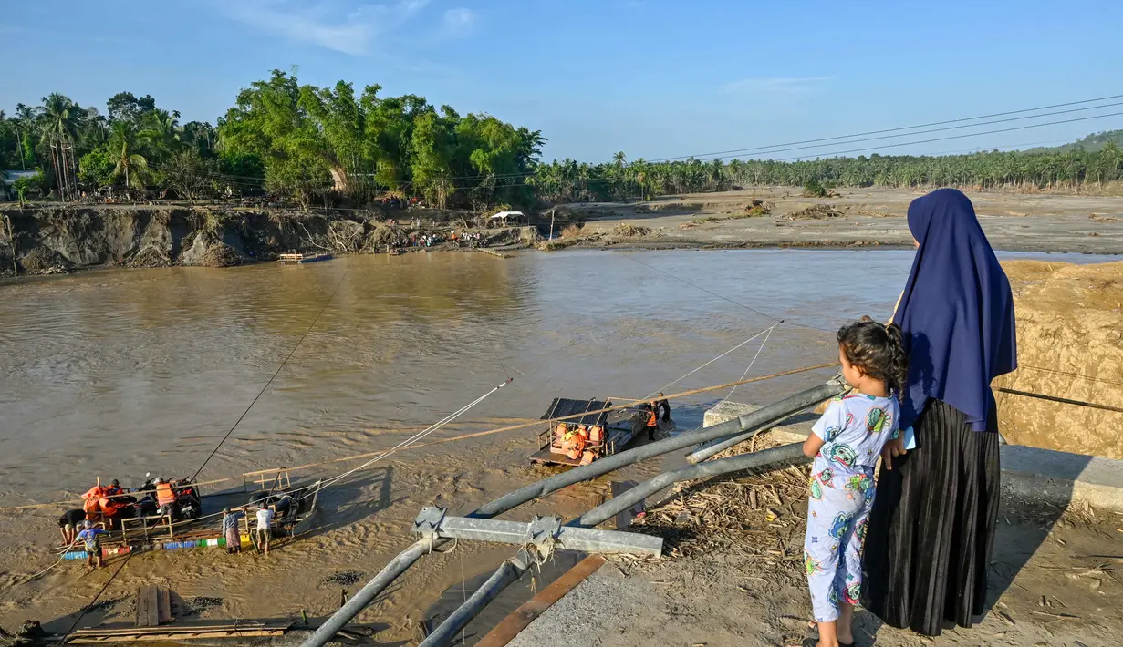 Dan, TNI AD, mulai Januari 2026, menargetkan pembangunan sekitar 50 jembatan darurat (Bailey), di Aceh dan wilayah lain yang terdampak, untuk menggantikan penyeberangan tali yang berisiko tinggi. Tampak dalam foto, seorang wanita dan anaknya melihat orang-orang menggunakan rakit tali penyeberangan untuk menyeberangi Sungai Peusangan setelah banjir bandang yang menghancurkan desa-desa di sekitarnya di Kabupaten Bireuen, provinsi Aceh, pada Senin 5 Januari 2026. (CHAIDEER MAHYUDDIN/AFP)
