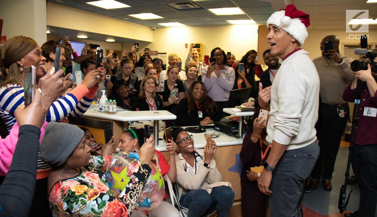 Mantan Presiden AS, Barack Obama mengunjungi Children's National Medical Center di Washington, Rabu (19/12). Dengan topi khas merah putih ala sinterklas, Obama membagikan hadiah natal untuk anak-anak yang sedang menjalani perawatan. (Chuck Kennedy / AFP)