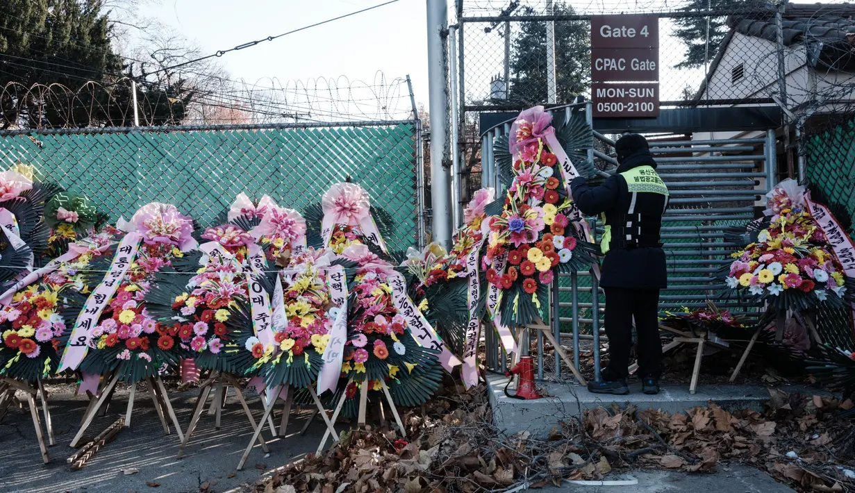 Seorang pekerja publik mengikat karangan bunga buatan dengan pesan-pesan dukungan untuk Presiden Korea Selatan yang dimakzulkan, Yoon Suk Yeol, di Seoul pada Kamis 9 Januari 2025. (Yasuyoshi CHIBA/AFP)