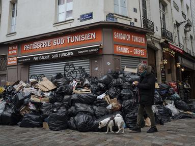 Seorang pria berjalan melewati tumpukan sampah di Paris, Senin (13/3/2023). RUU kontroversial yang akan menaikkan usia pensiun di Prancis dari 62 menjadi 64 tahun mendapat dorongan dengan adopsi tindakan Senat di tengah pemogokan, protes, dan sampah yang tidak diambil menumpuk semakin tinggi dari hari ke hari. (AP Photo/Lewis Joly)