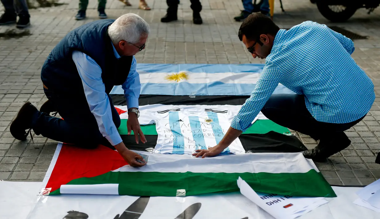 Aktivis pro-Palestina menempelkan jersey timnas Argentina yang bertuliskan ungkapan terima kasih dengan bendera nasional Palestina di Barcelona (6/6). (AFP Photo/Pau Barrena)