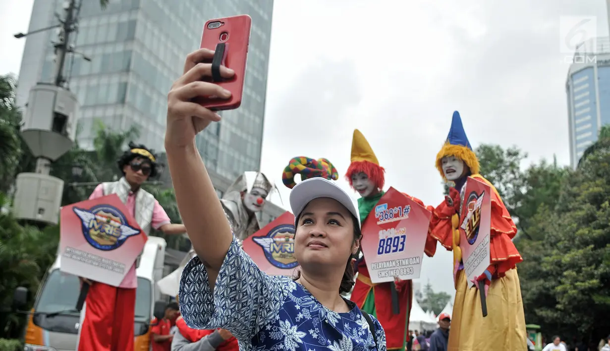 Warga berswafoto bersama badut yang tengah menyosialisasikan sistem tilang Electronic Traffic Law Enforcement (ETLE) kepada pengunjung car free day (CFD) di Bundaran HI, Jakarta, Minggu (25/11). (Merdeka.com/Iqbal Nugroho)