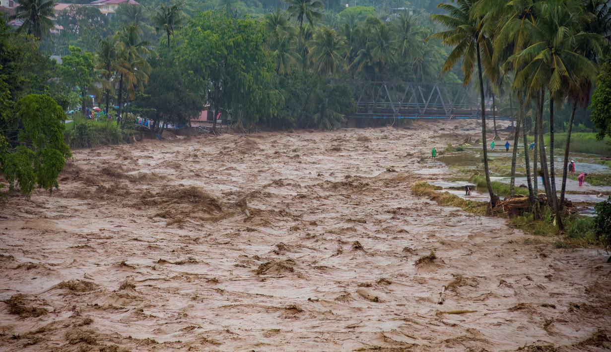 Data Pusat Pengendalian Operasi Penanggulangan Bencana (Pusdalops) BPBD Padang, Kecamatan Koto Tangah menjadi wilayah dengan jumlah terdampak terbesar, yaitu 20.983 warga. Tampak dalam foto, warga bertahan di tepi sungai saat banjir melanda Padang, Provinsi Sumatra Barat, pada Kamis 27 November 2025. (REZAN SOLEH/AFP)