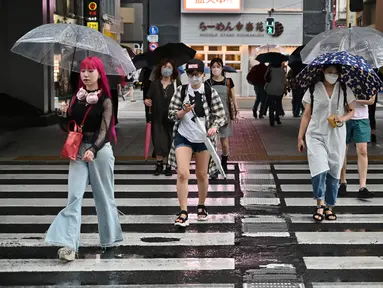 Orang-orang menyeberang di bawah rel kereta api selama hujan yang terisolasi di distrik Akihabara Tokyo (13/8/2022). Hujan lebat yang dibawa oleh Badai Tropis Meari melanda daerah tersebut. (AFP/ Richard A. Brooks)