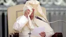 Paus Fransiskus berusaha menyibak mantel yang menutupi wajahnya ketika memberikan ceramah pada acara audiensi umum di Lapangan Santo Petrus, Vatikan, Rabu (16/5). Jubah Paus berkali-kali diterbangkan oleh angin. (AP Photo/Alessandra Tarantino)