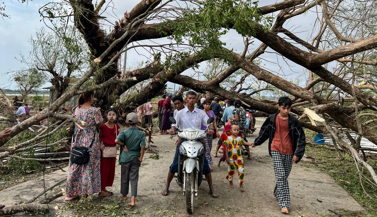 Warga berjalan melewati pohon tumbang setelah Topan Mocha mendarat di Kyauktaw di negara bagian Rakhine Myanmar, Senin (15/5/2023). (Photo by Sai Aung MAIN / AFP)