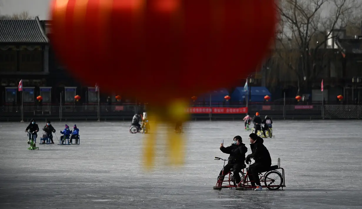 Sepasang warga menggunakan ponsel untuk berswafoto saat menaiki kereta luncur di danau beku di Beijing pada Selasa (12/1/2021). Ketika musim dingin tiba, danau di Beijing banyak yang membeku dan dijadikan area ice skating musiman. (Photo by WANG Zhao / AFP)