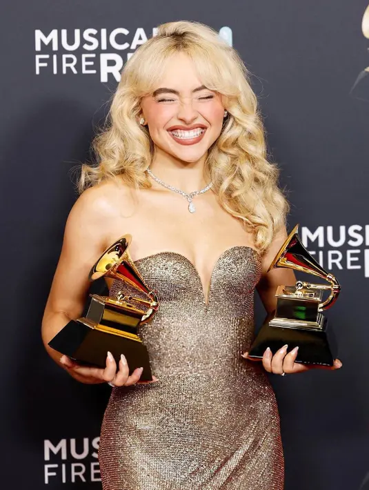 Saat naik ke atas panggung untuk menerima trofi, ia tampil anggun dengan gaun strapless panjang yang dihiasi perhiasan, dilengkapi dengan kalung berlian dan cincin besar yang serasi. [@sabrinacarpenter/@mtv].