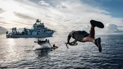 Menggunakan kapal selam Neptune milik organisasi nirlaba OceanX di perairan lepas pantai Pulau Sulawesi. Tampak dalam foto yang diambil pada 9 Januari 2026, menunjukkan awak kapal OceanXplorer, sebuah kapal penelitian yang dioperasikan oleh organisasi nirlaba kelautan OceanX, melompat ke laut dari sebuah perahu untuk berenang menuju kapal selam yang muncul ke permukaan dan memasang tali penyelamat di perairan lepas pantai Pulau Sulawesi. (YASUYOSHI CHIBA/AFP)