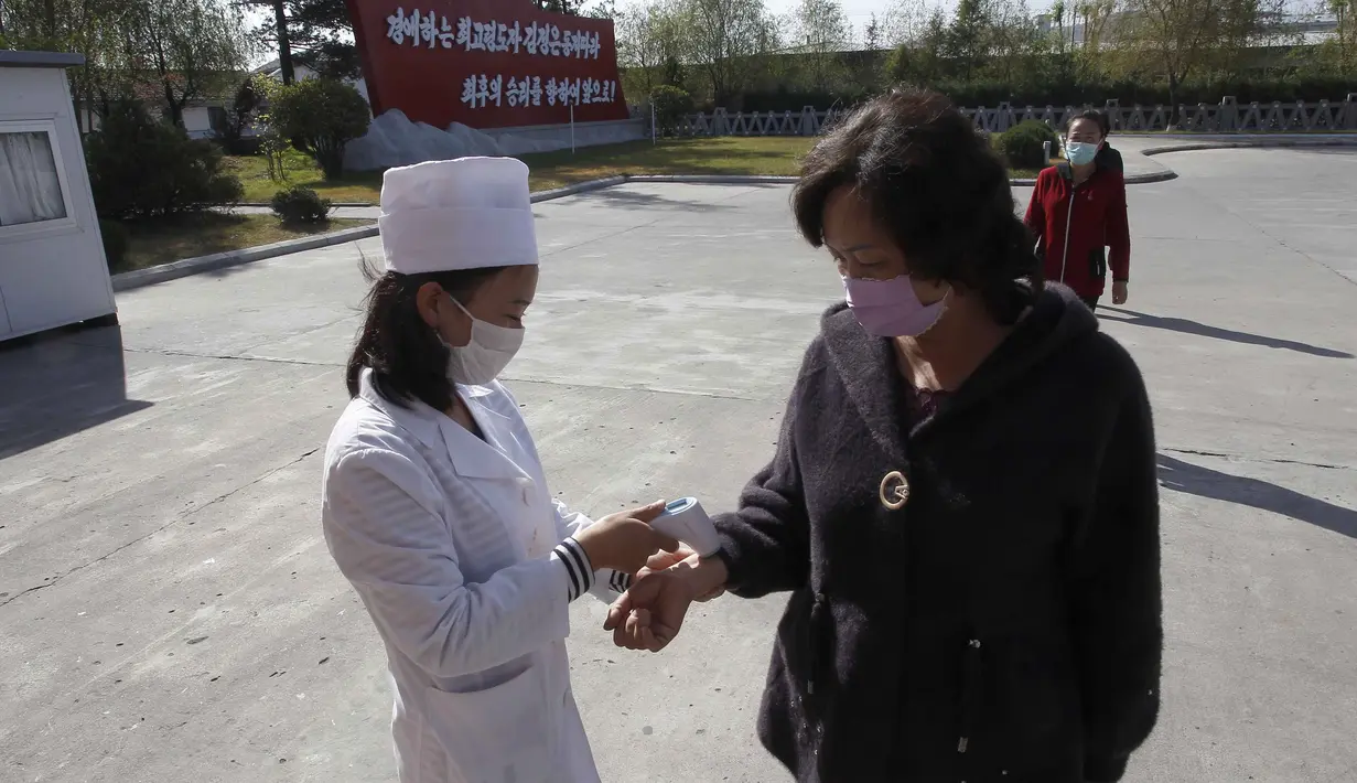 Petugas higienis dan anti wabah memeriksa suhu tubuh perempuan di pintu gerbang Pabrik Sepatu Kulit Wonsan di Wonsan, Provinsi Kangwon, Korea Utara pada 28 Oktober 2020. (AP Photo/Jon Chol Jin)